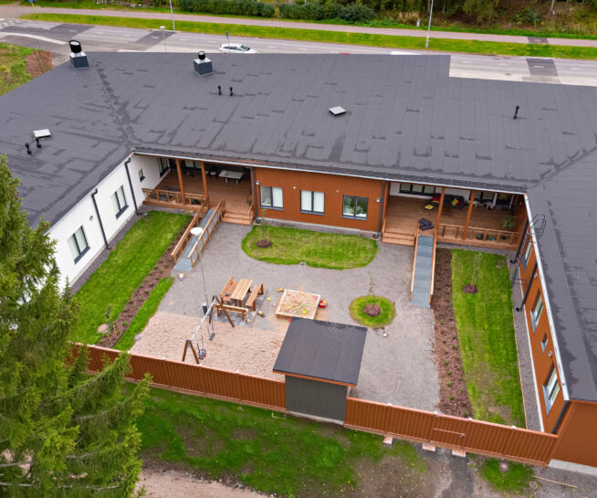 Aerial view of a building with a sandbox, swing and table set in the yard.