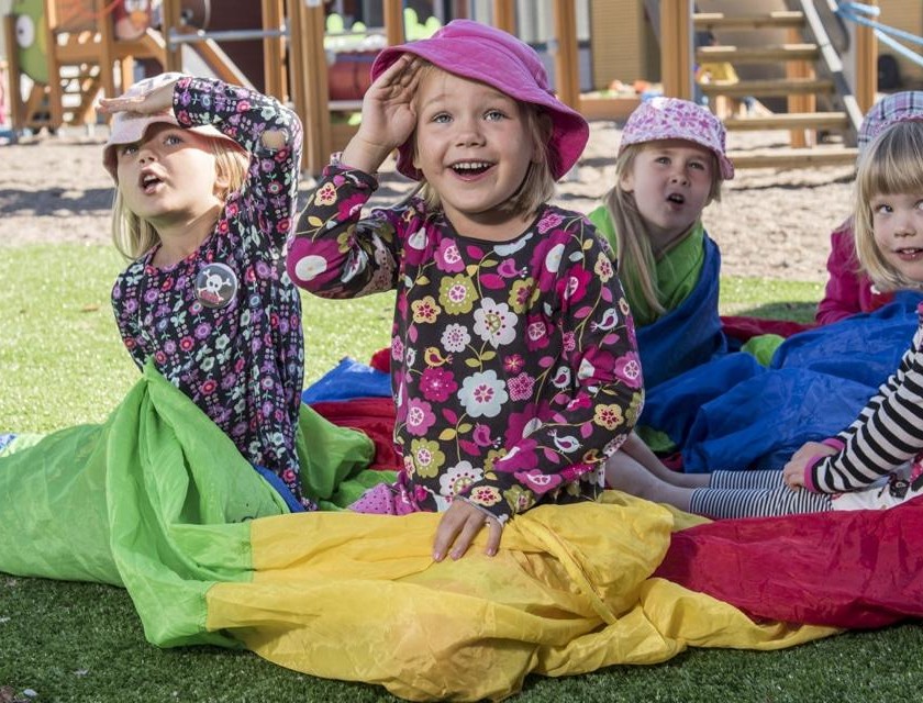 Lapset istuvan pihalla värikkään kankaan päällä ja katsovat kameran yli